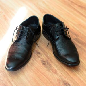 A pair of stylish black leather dress shoes with laces on a wooden floor, highlighting their elegance and design.