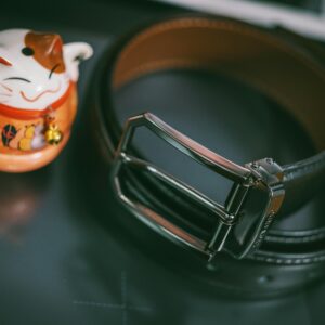 Elegant black leather belt beside a traditional Japanese maneki-neko, symbolizing luck and fortune.